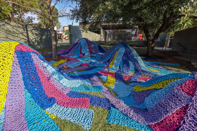 Photograph of Stomping Ground by Orly Genger an interactive sculpture on site at the McNay, omposed from brightly painted recycled lobster rope.